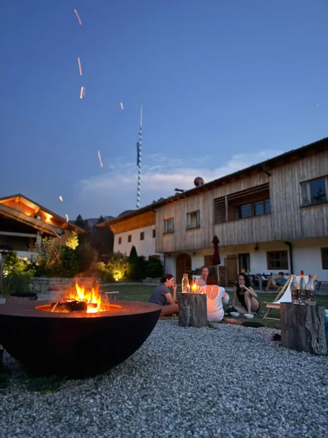 Feuerschale am Abend auf einem Kiesplatz vor einem Holzhaus, am Himmel noch Restlicht