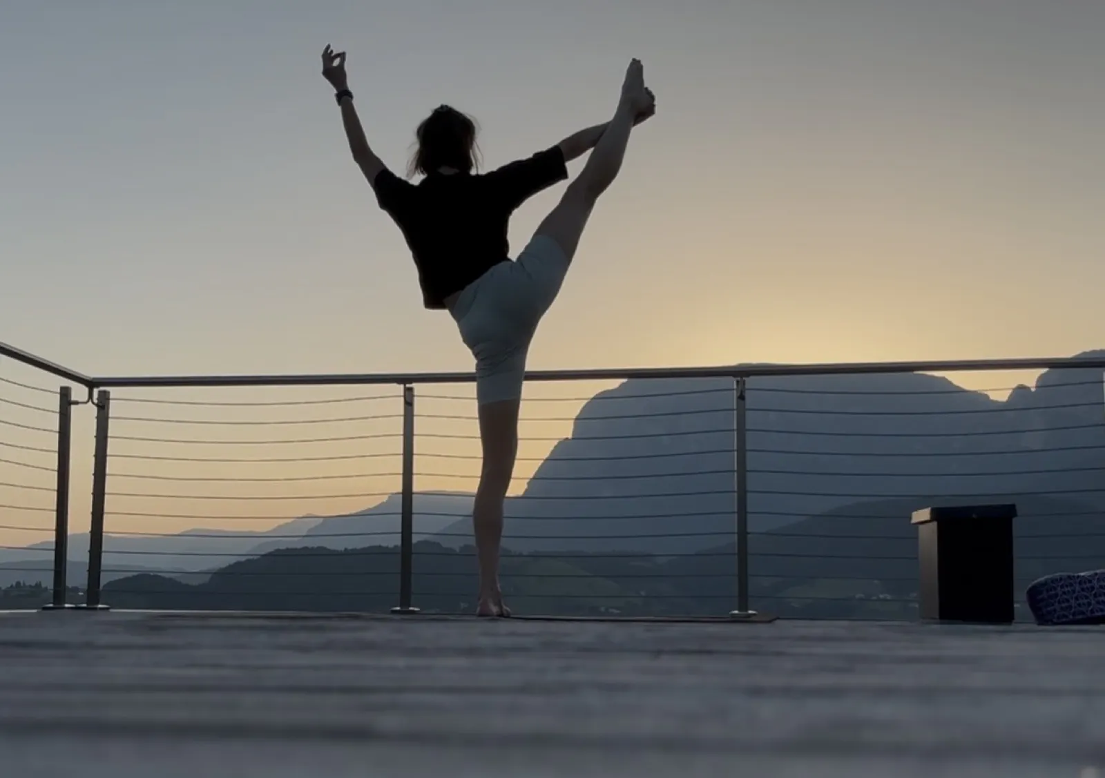 Silhouette einer Person im Yoga-Handstand vor Dämmerungshimmel und Bergen auf einer Terrasse