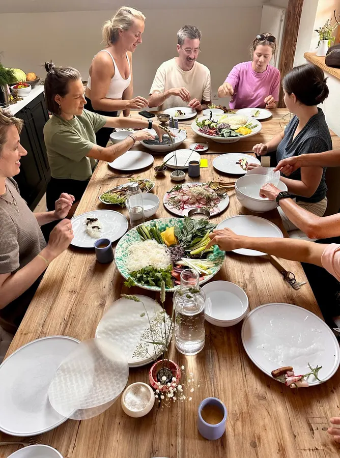 Eine Gruppe isst an einer langen Holztafel mit vielen Schalen und Tellern