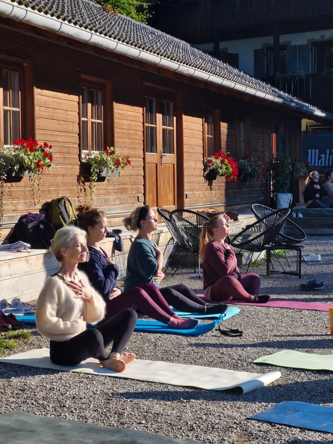 Yoga-Gruppe auf Matten vor dem Holzhaus des Waldhauses, im Sommer aufgenommen